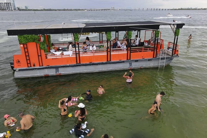 A party boat anchored, with a number of people on both the deck and in the water